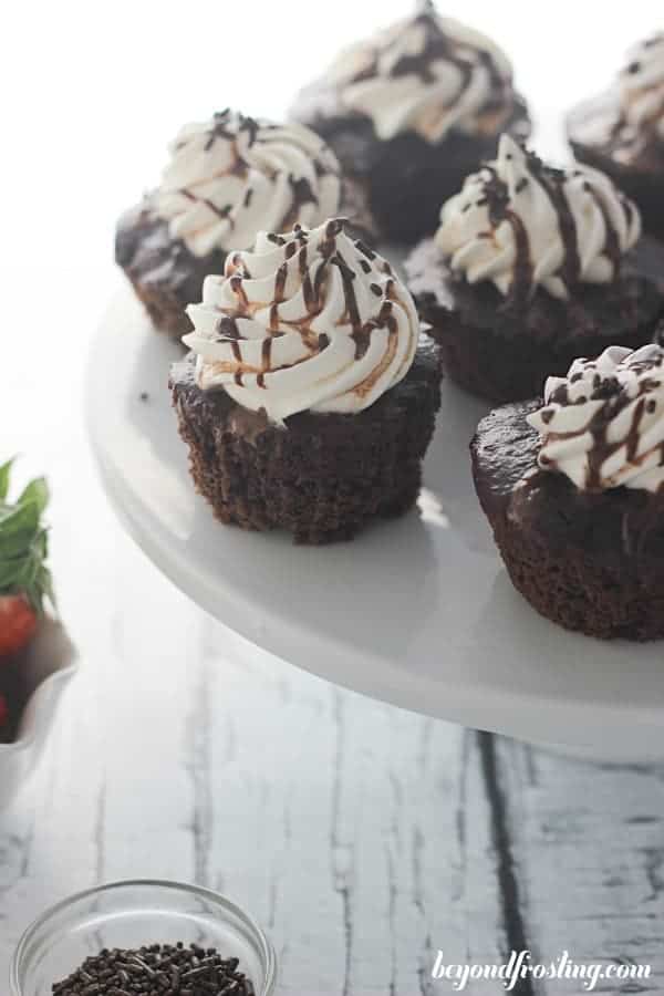 A white cake stand with chocolate cupcakes and white frosting