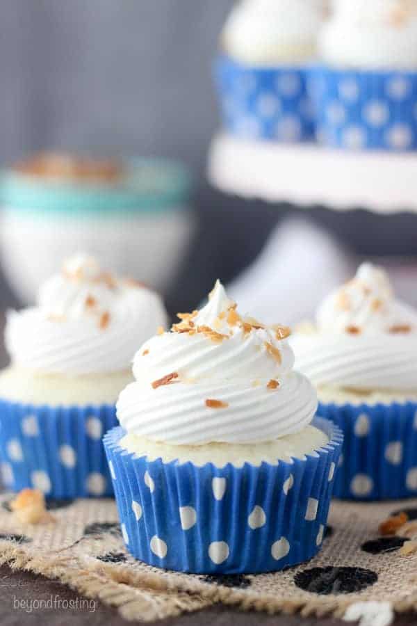 Three pretty cupcakes with bright blue polka dot wrappers and some toasted coconut on top