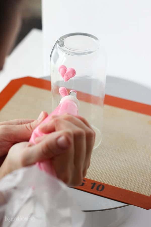 A clear juice glass with pink hearts piped with buttercream frosting