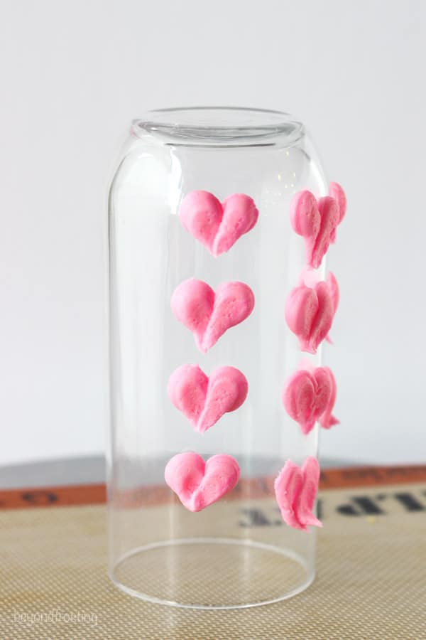 A clear juice glass with pink hearts piped with buttercream frosting