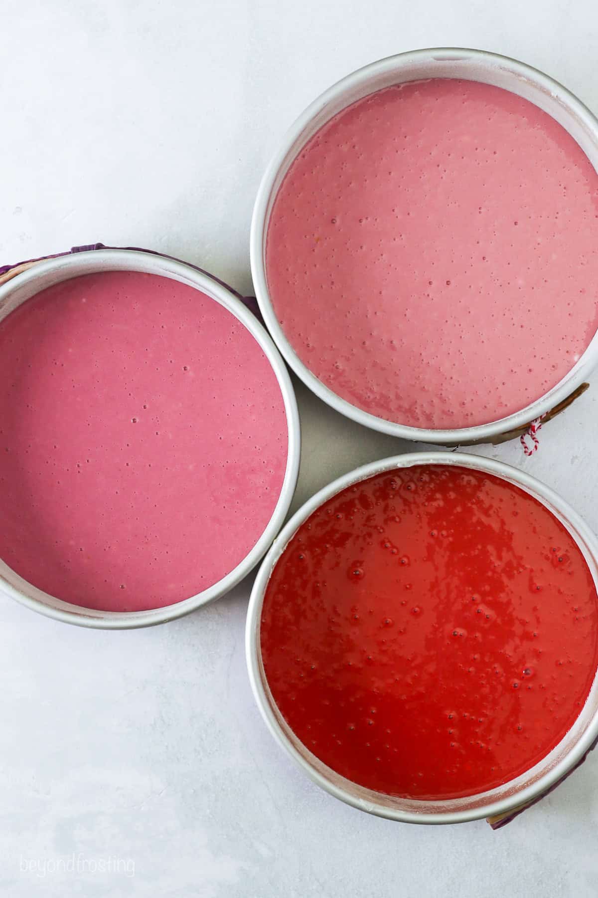 Overhead view of three cake pans filled with ombre batter in shades of red and pink.