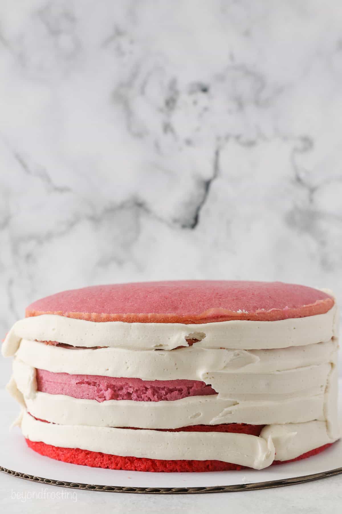 Side view of a red and pink ombre layer cake partially covered in vanilla frosting.