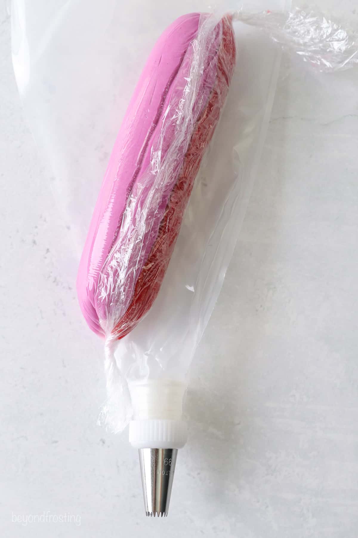 Red and pink ombre frosting rolled up inside a piece of plastic wrap, on top of a piping bag fitted with a piping tip.