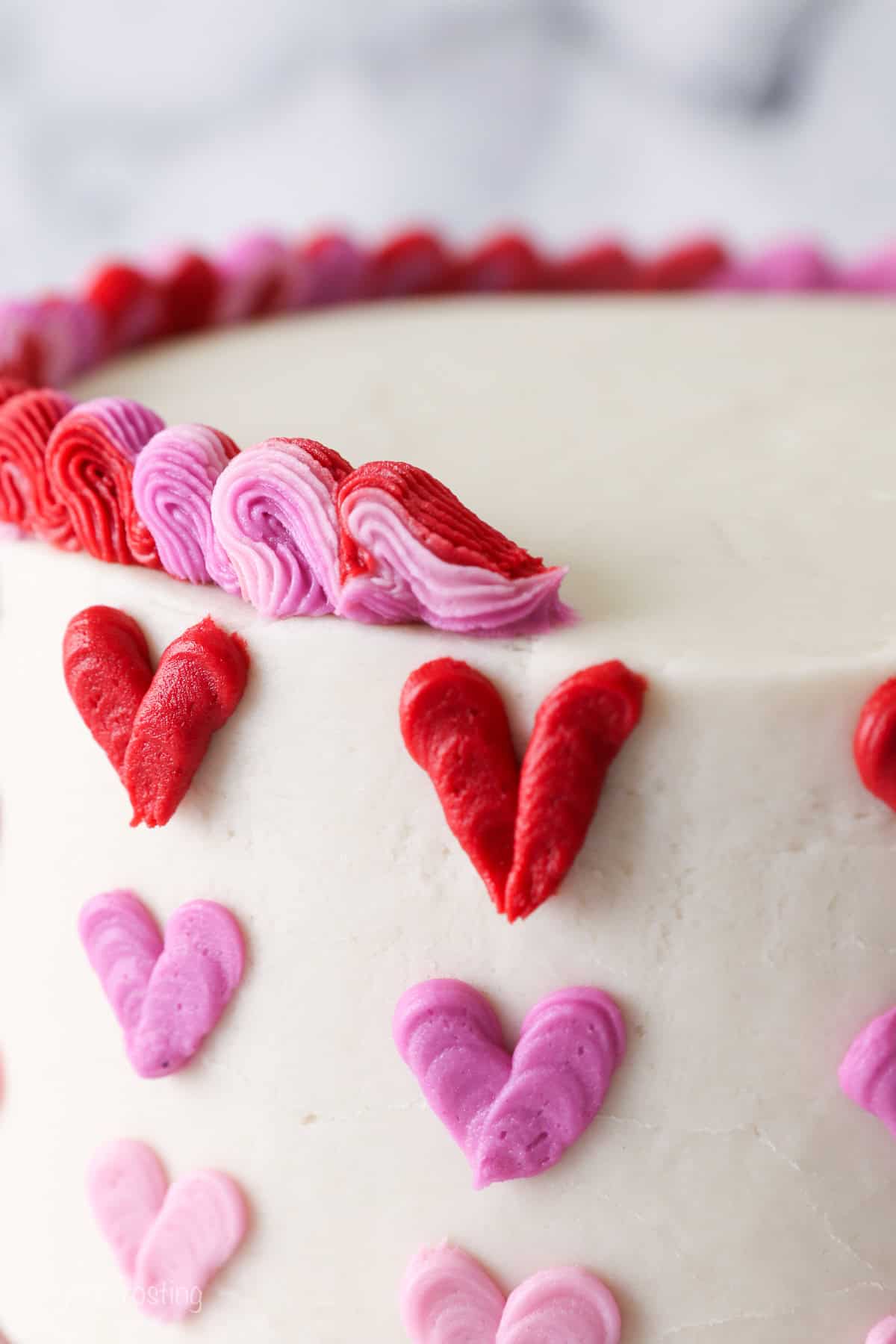 Close up of piped red and pink ombre frosting on top of a cake decorated with red and pink ombre hearts.