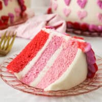 A slice of Valentine's Day ombre cake on a plate with the rest of the cake in the background.