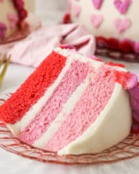 A slice of Valentine's Day ombre cake on a plate with the rest of the cake in the background.