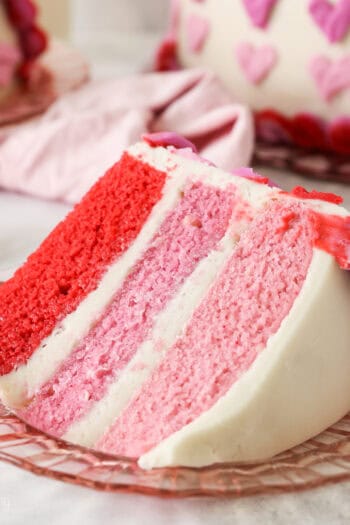 A slice of Valentine's Day ombre cake on a plate with the rest of the cake in the background.