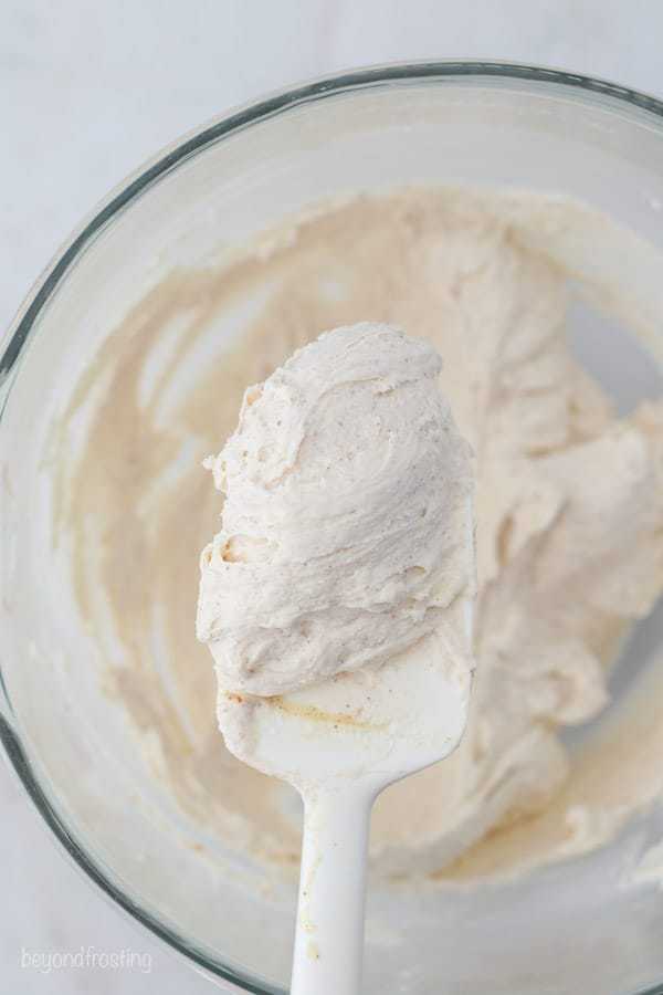 A white spatula with a dollop of brown butter frosting being held over the mixing bowl