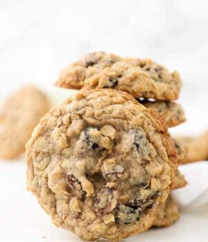 A stack of oatmeal raisin cookies and one big cookie is leaning up against the stack showing the raisins on top