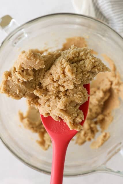Overhead view of a red rubber spatula scooping creamed butter and sugar from a mixer bowl.