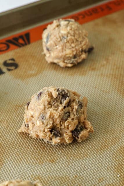 Scoops of oatmeal raisin cookie dough on a silpat-lined baking sheet.