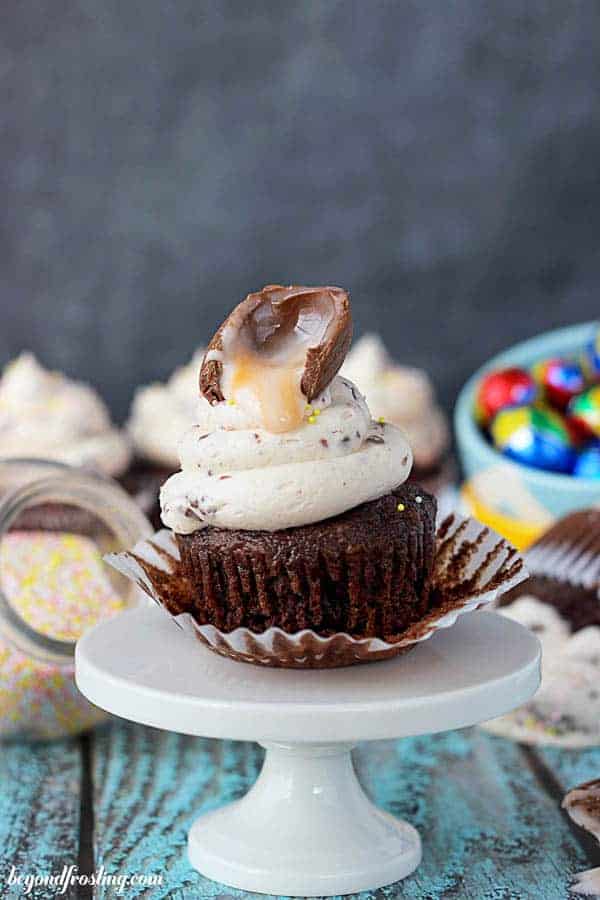 A gooey Cadbury egg dripping onto a frosted cupcake on top of a mini white cake stand