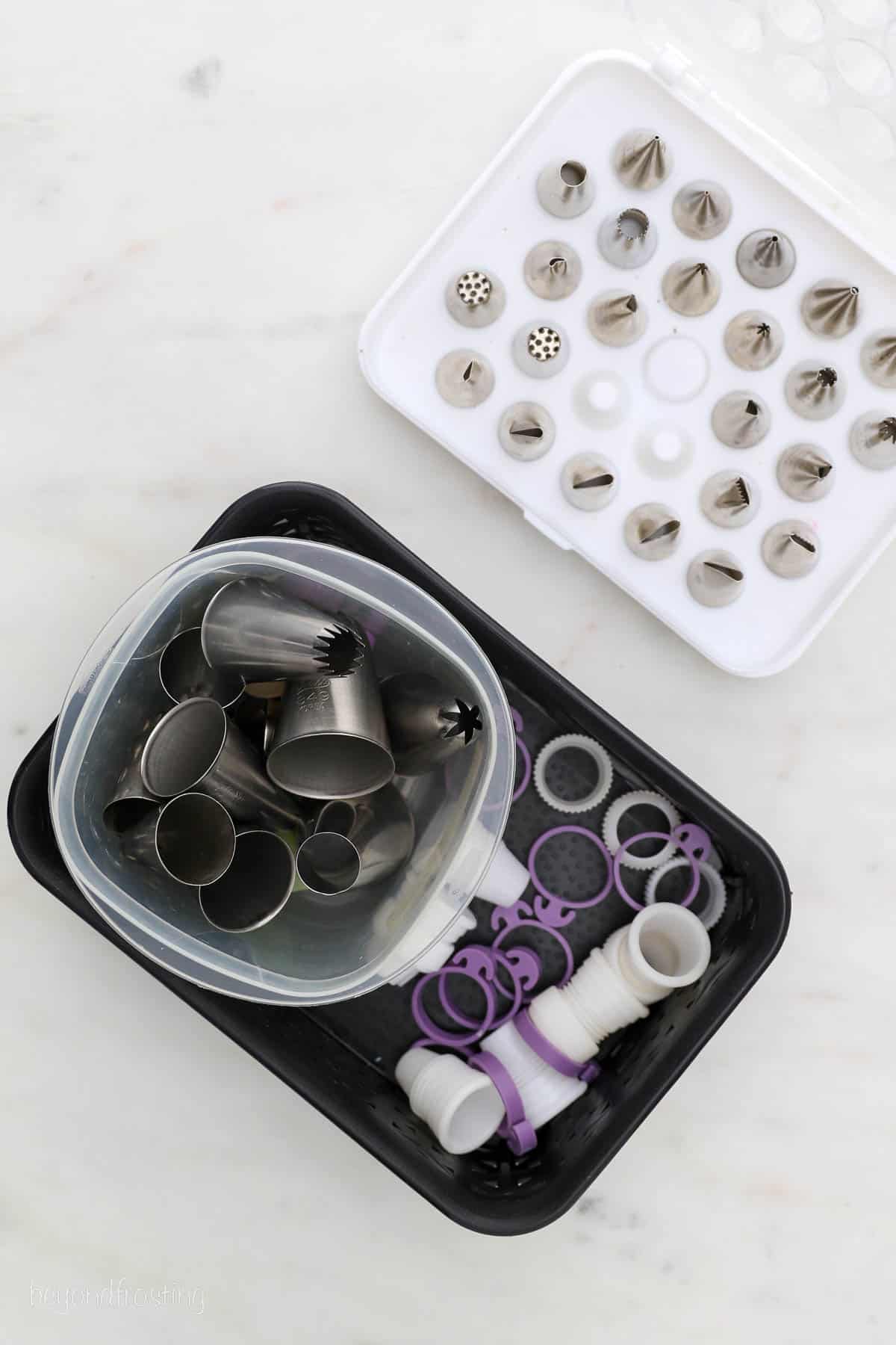 Overhead view of piping tips arranged on an organizing rack, next to a black container filled with more piping tips and couplers.