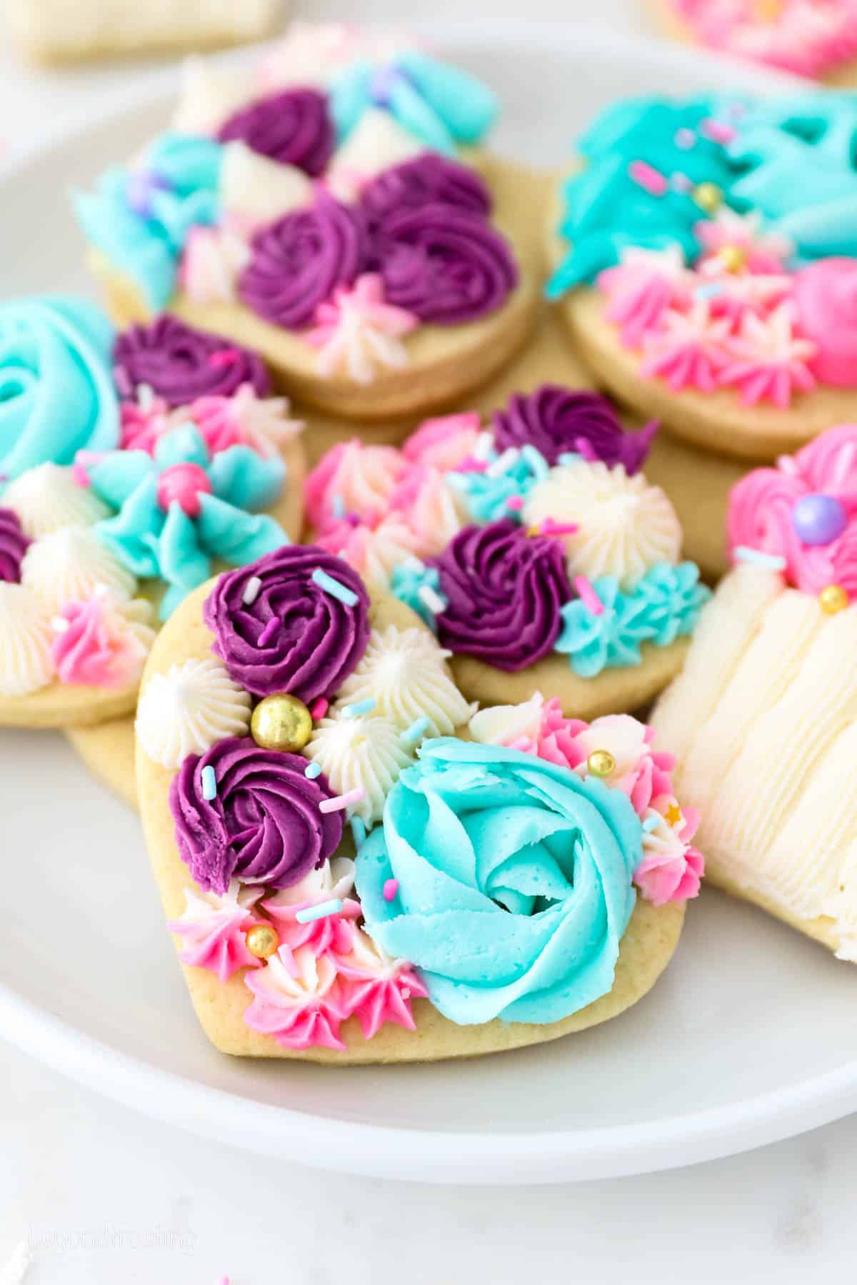 A plate of sugar cookies decorated with purple, teal, white, and pink buttercream frosting.