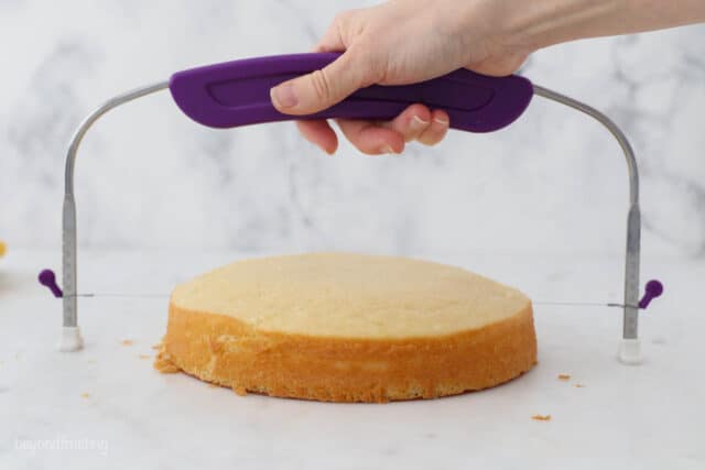 A hand holding a cake level over a domed vanilla cake layer on a countertop.