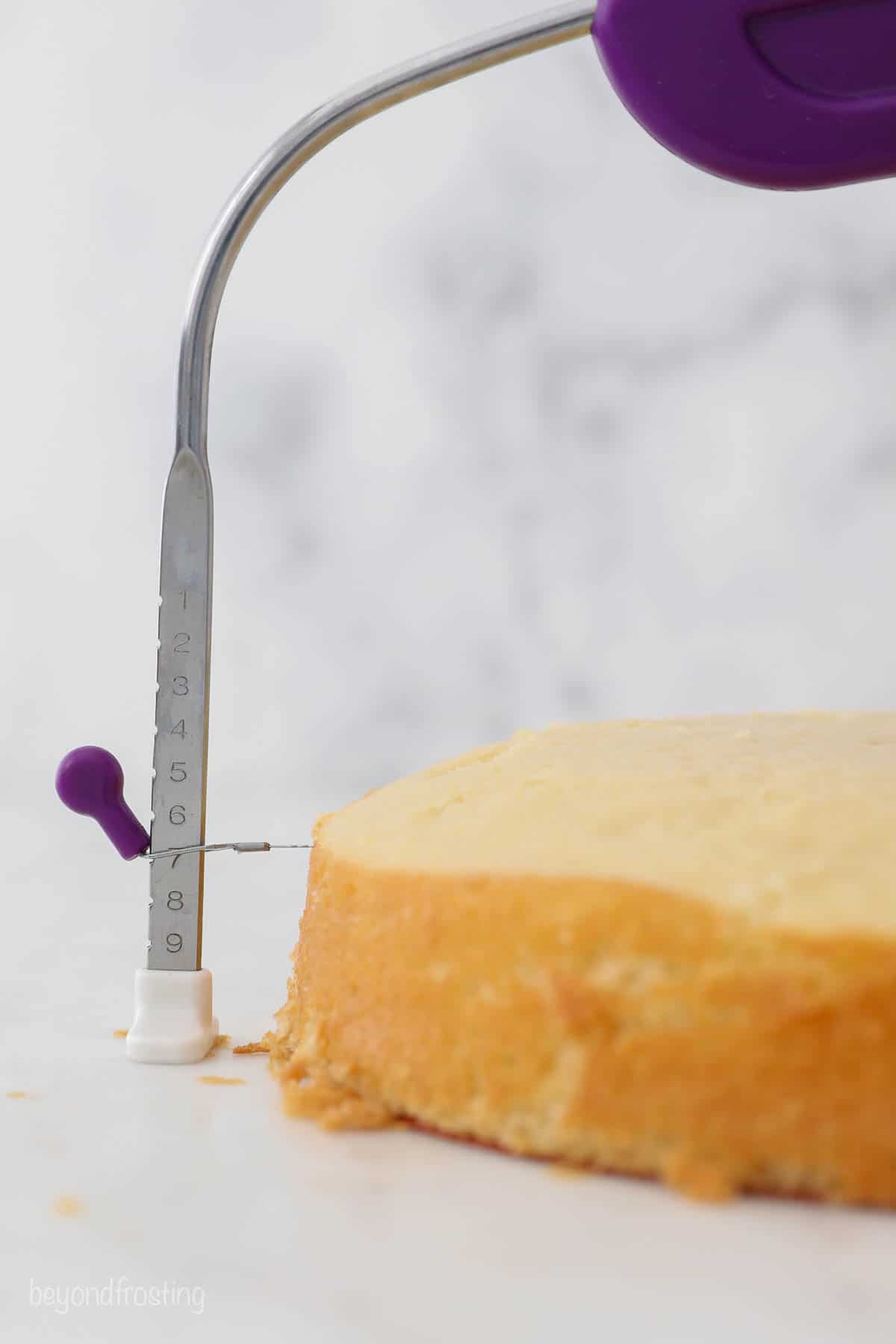 Close up of a cake level trimming the dome from the top of a vanilla cake layer.