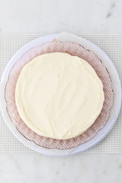 Overhead view of the first vanilla cake layer topped with a smoothed-out layer of vanilla frosting.