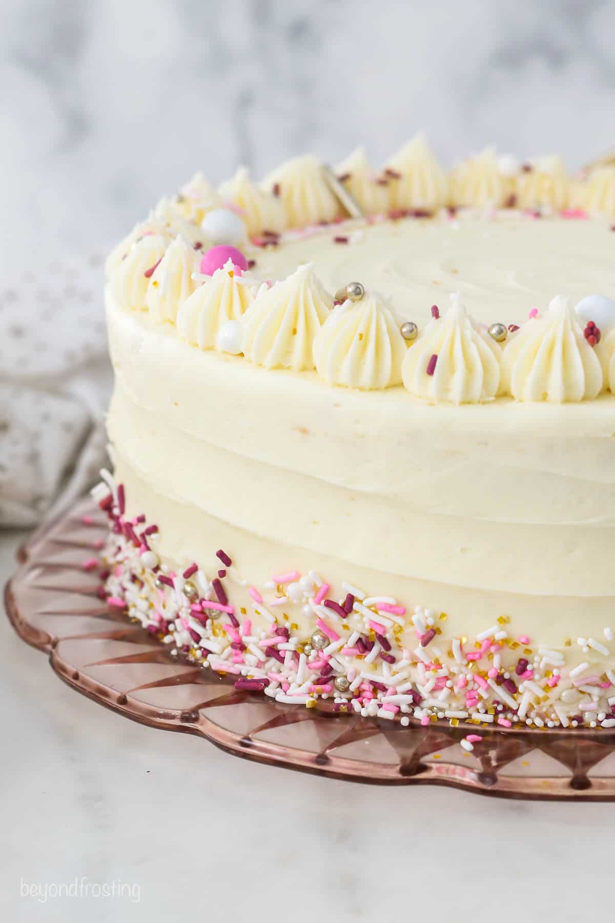 A finished frosted layer cake decorated with a crown of frosting swirls and rainbow sprinkles.