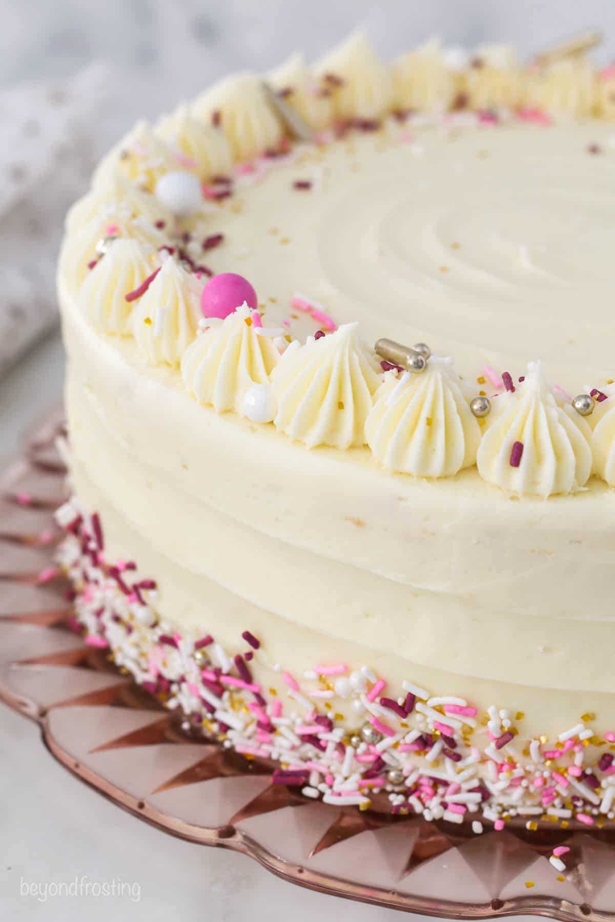 A finished frosted layer cake decorated with a crown of frosting swirls and rainbow sprinkles.