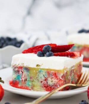 A slice tye dye poke cake with patriotic colors and berry topping
