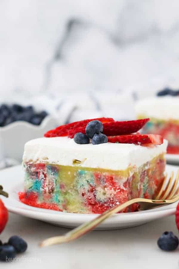 A slice tye dye poke cake with patriotic colors and berry topping