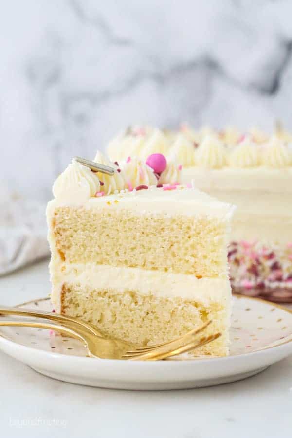 A slice of vanilla cake with pink sprinkles on a gold polka dot plate
