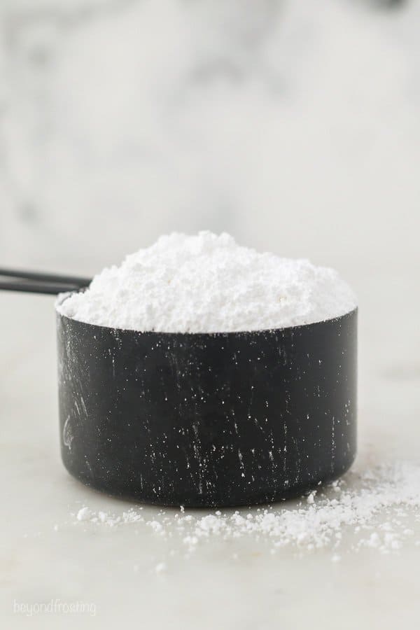 A black measuring cup filled with powdered sugar