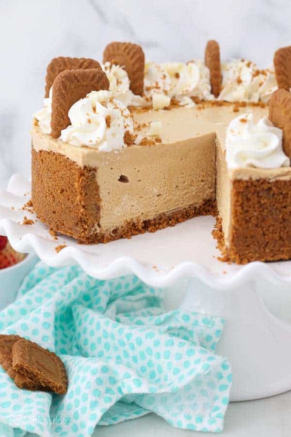 A white cake plate with no-bake cheesecake decorated with Biscoff cookies, a slice it cut out
