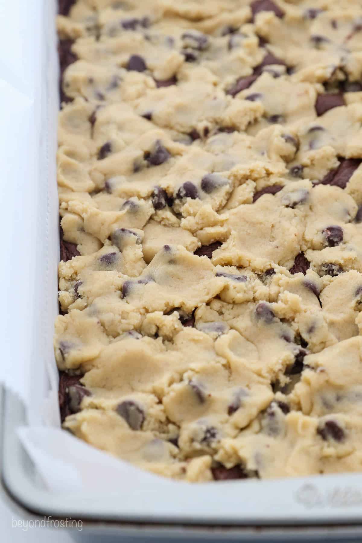 Close up of cookie dough spread on top of brownie batter in a pan