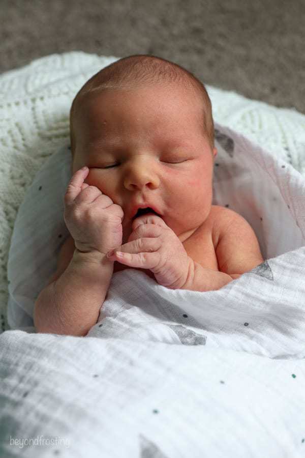 a baby wrapped in a swaddle blanket with his hands in his face