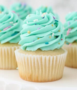 Gluten-free vanilla cupcakes frosted with bright mint-colored frosting swirls and topped with sprinkles.