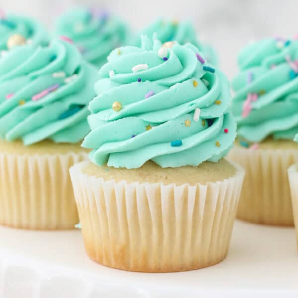 Gluten-free vanilla cupcakes frosted with bright mint-colored frosting swirls and topped with sprinkles.