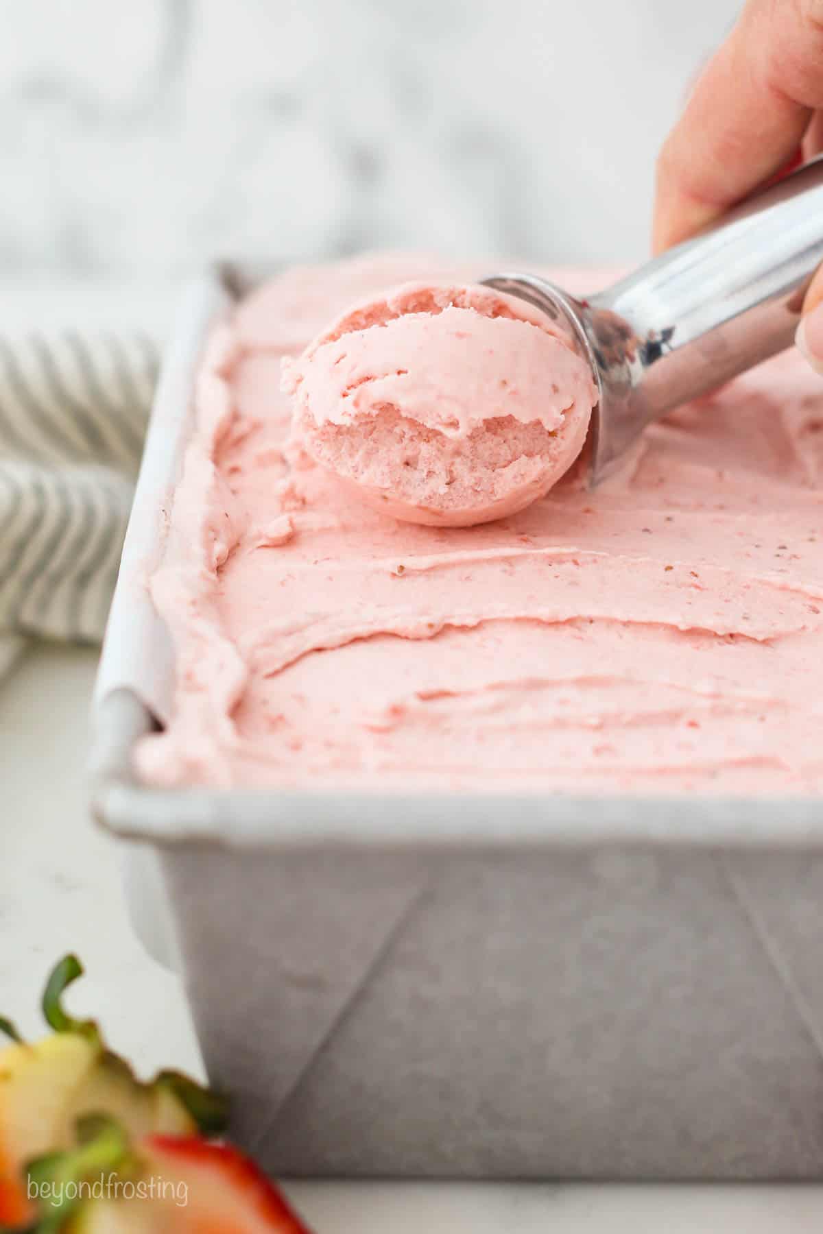 An ice cream scoop scooping strawberry ice cream