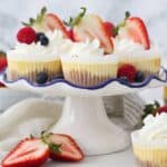 A white cake plate with mini cheesecake topped with Strawberries