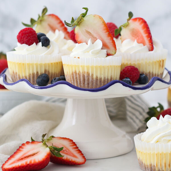 A white cake plate with mini cheesecake topped with Strawberries