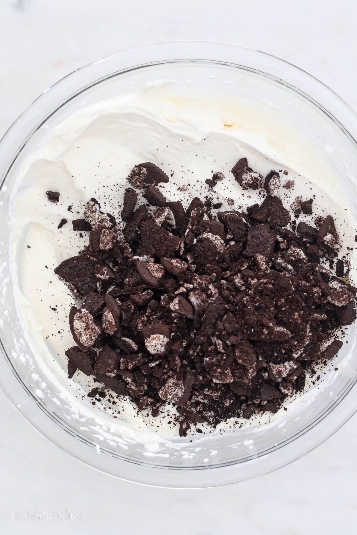 Crushed Oreos added to a bowl with cream cheese ice cream base.