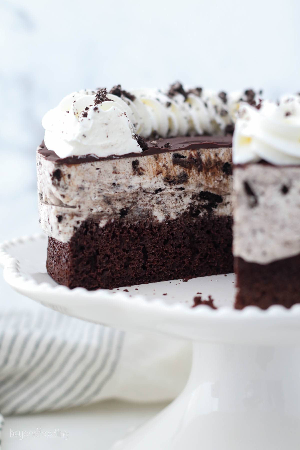 Oreo ice cream cake topped with whipped cream on a cake stand, with a slice missing.