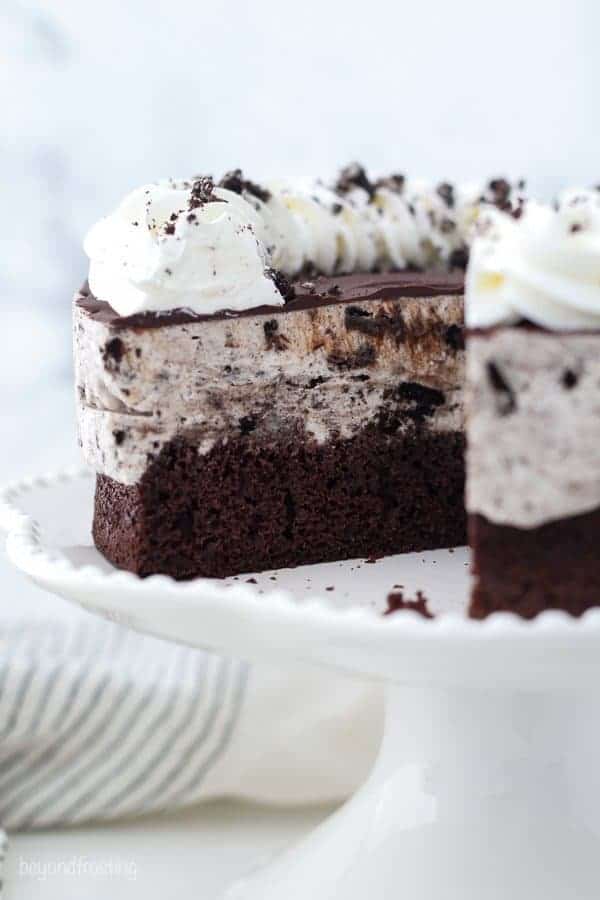 a white cake stand with an Oreo ice cream cake on top, a slice is missing