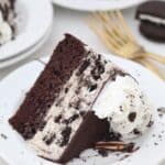a slice of Oreo ice cream cake on a white plate- a layer of chocolate cake and a layer of oreo ice cream