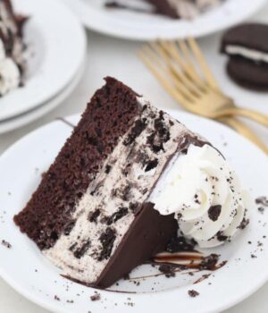 a slice of Oreo ice cream cake on a white plate- a layer of chocolate cake and a layer of oreo ice cream