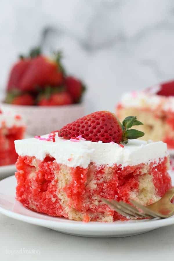 A slice of Strawberry poke cake on a white plate with a couple bites taken out of it