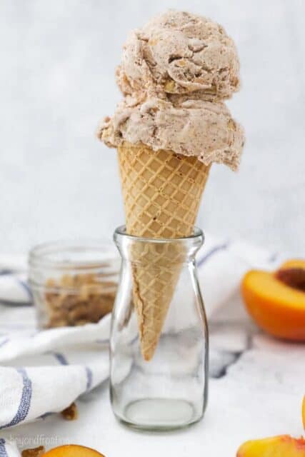 A small glass jar with an ice cream cone with two scoops of peach ice cream