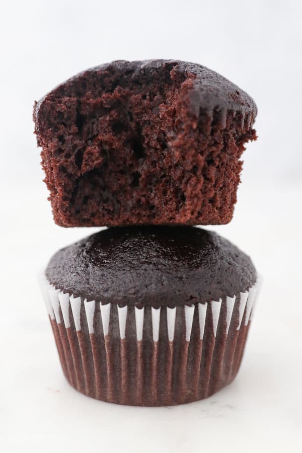 two unfrosted chocolate cupcakes stacked, the top one has a bite missing