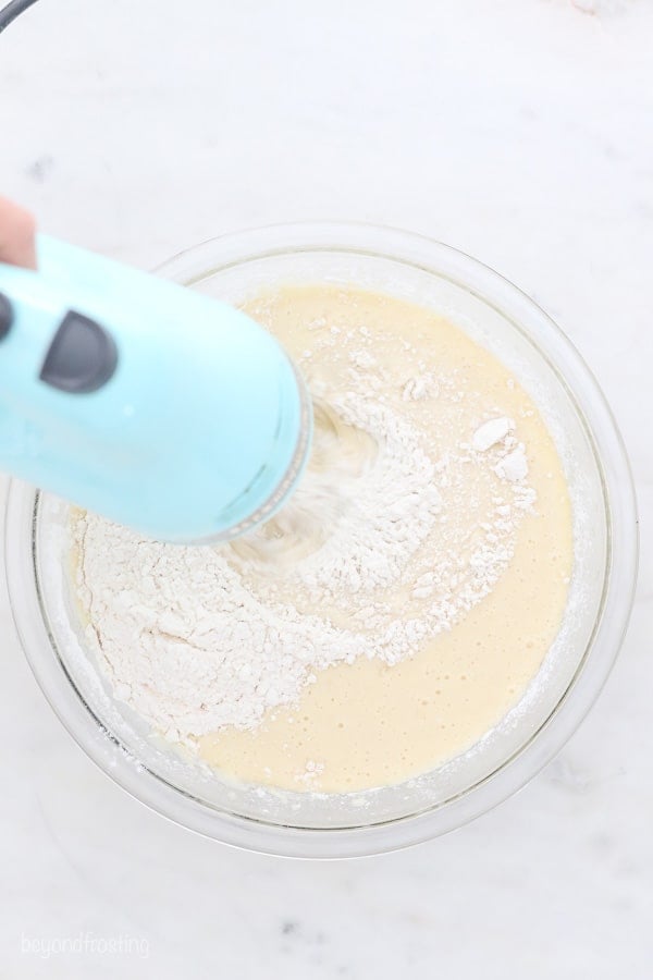 an overhead shot of a glass mixing bowl and a teal hand mixer