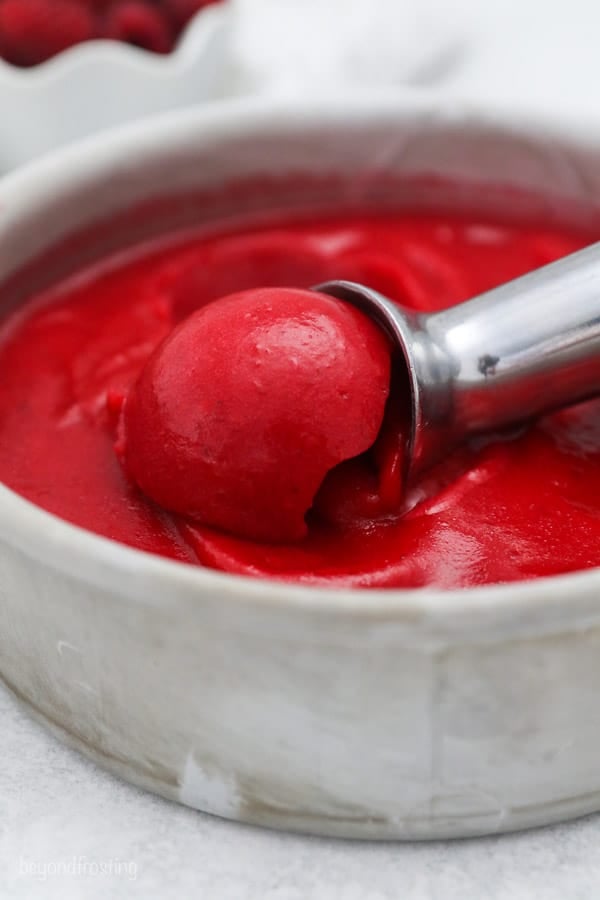 a cake pan with raspberry sorbet and an ice cream scoop digging through it