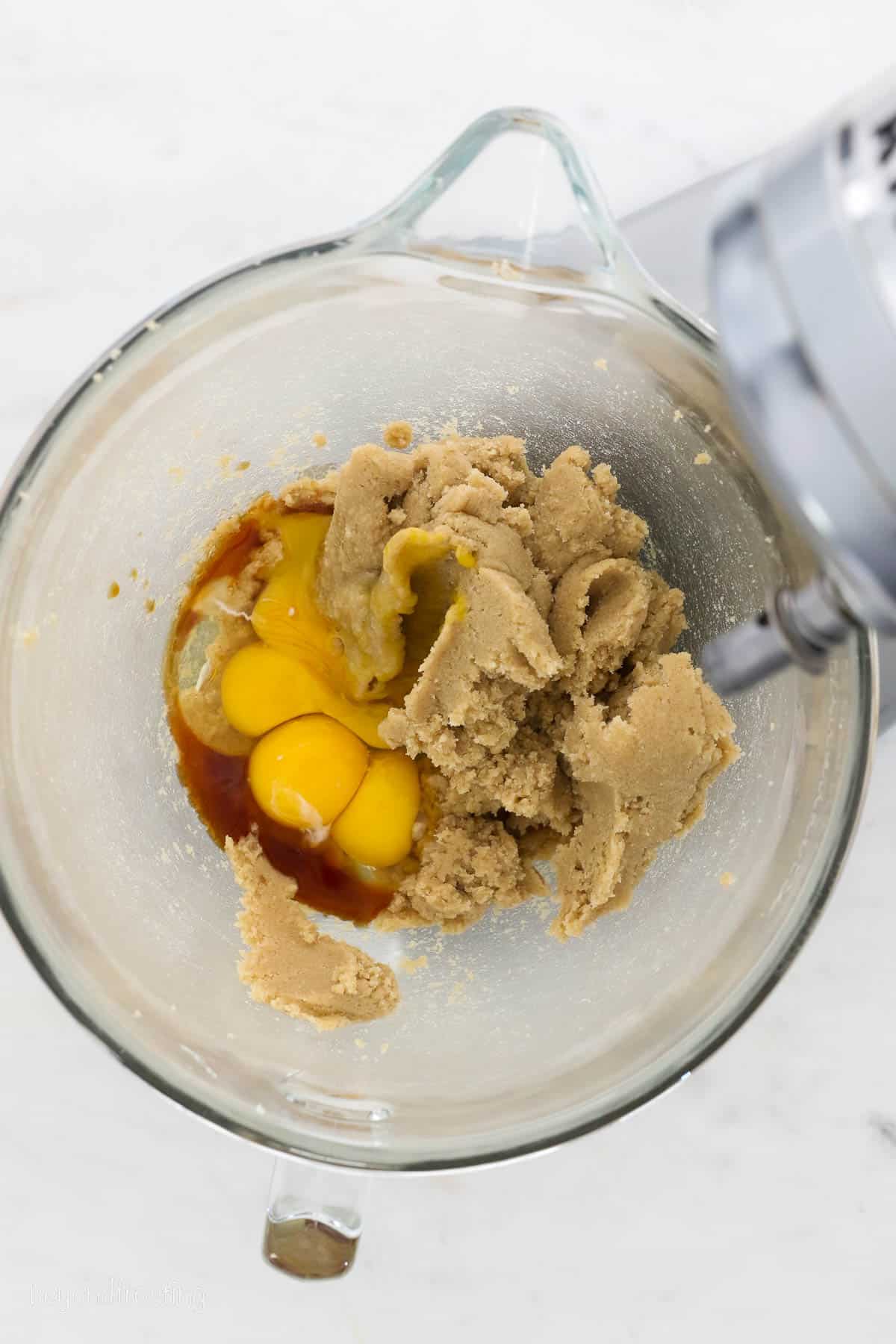 Eggs and vanilla added to creamed butter and sugar in a glass bowl.