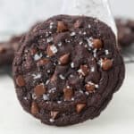 A giant chocolate cookie sprinkled with flaked sea salt leaning against a glass of milk.
