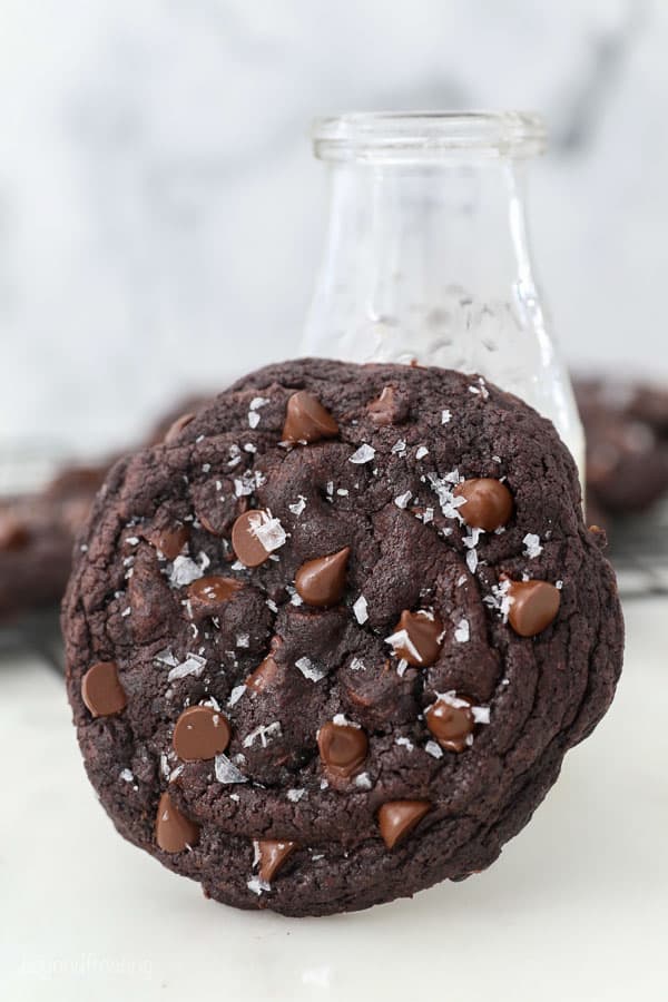 A large chocolate cookie leaning up against a glass of milk