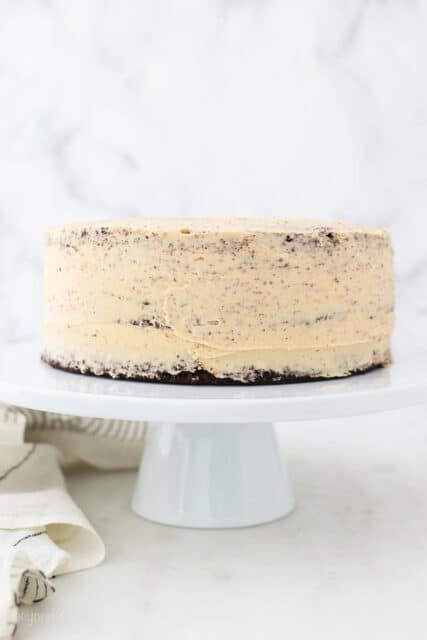 Chocolate peanut butter layer cake frosted with a crumb coat on a white cake stand.