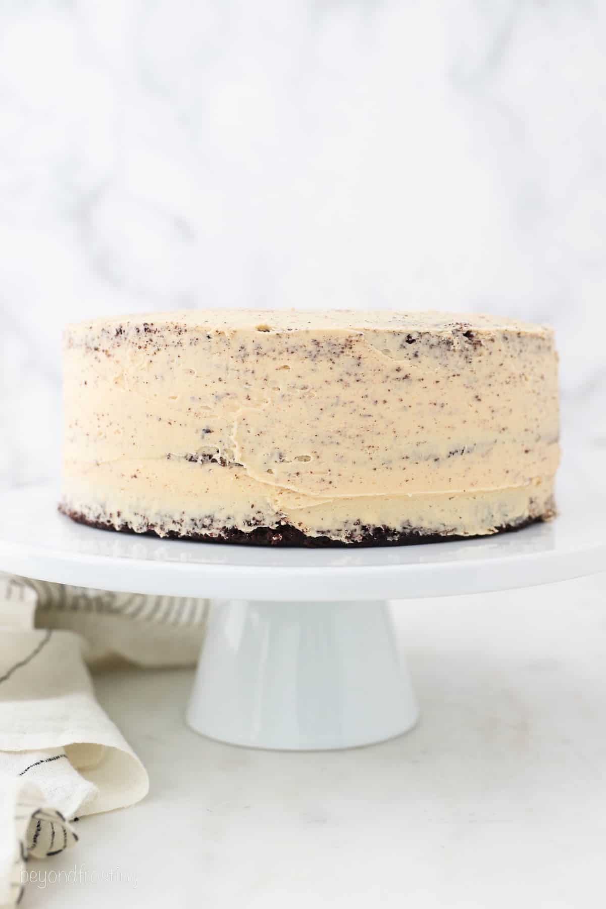 Chocolate peanut butter layer cake frosted with a crumb coat on a white cake stand.